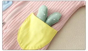 Detail of pink waffle knit baby romper featuring yellow pocket and green ear accents
