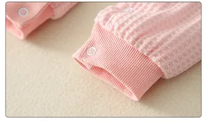 Detail of pink waffle knit baby romper featuring soft ribbed cuffs and white snap buttons
