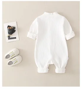 Back view of a white ribbed cotton newborn romper with rolled cuffs on beige background