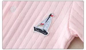 Close-up of pink cotton knit baby romper with sailboat embroidery and white snaps