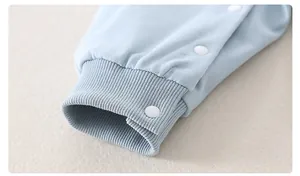 Close-up of light blue cotton baby romper sleeve with ribbed cuff and white resin snap button
