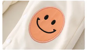 Detail eines Baby-Baumwoll-Stramplers mit orangefarbenem Smiley-Patch und Druckknöpfen