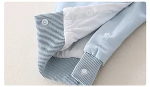 Close-up of cotton baby romper featuring blue ribbed cuffs and secure white resin snap buttons