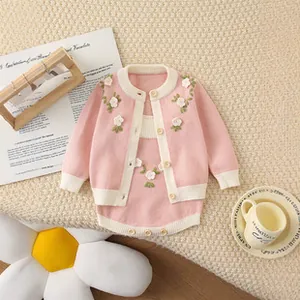 Close-up of pink knitted baby set featuring white floral embroidery and cotton cardigan