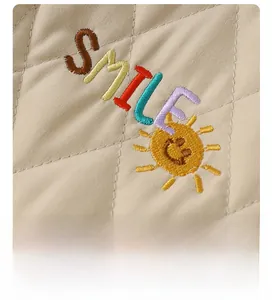Macro detail of smiley face embroidery on quilted beige cotton fabric for baby rompers