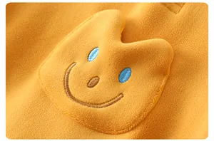 Detailed macro view of yellow fleece baby romper featuring a 3D plush smiley embroidery