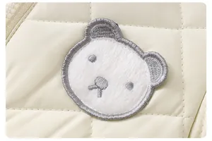 Dettaglio macro del tessuto trapuntato crema con ricamo a testa d'orso in peluche