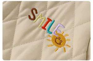 Macro detail of beige quilted baby romper fabric with SMILE embroidery and sun face