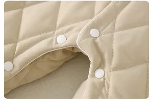 Detail of quilted beige baby romper showing diamond stitching and white plastic snaps