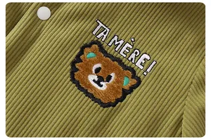 Detail of olive green corduroy fabric with cartoon bear embroidery and white snap buttons