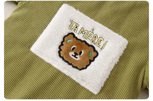 Detail of olive green corduroy fabric with a plush bear patch and embroidered text