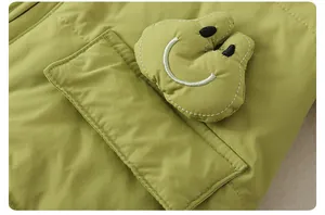 Detail of light green baby winter romper featuring a yellow plush smiley face pocket