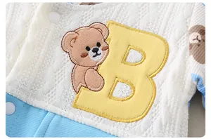 Detail of baby romper featuring knit texture, blue fabric, and bear embroidery with letter B