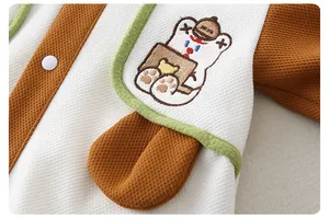 Detail of baby romper featuring waffle knit fabric, cartoon bear embroidery and snaps