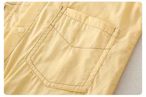 Detail eines gelben Baby-Bodys aus Baumwolle mit Kontrastnähten an Tasche und Druckknopf