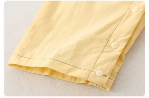 Makroaufnahme von gelbem Baumwollstoff mit drei weißen Druckknöpfen an einem Baby-Strampler