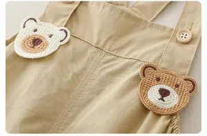 Détail d'une salopette bébé en coton kaki avec des oursons au crochet et un bouton