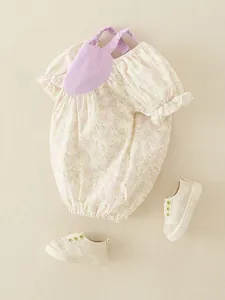 Floral baby girl bodysuit with purple straps and matching canvas shoes on beige fabric