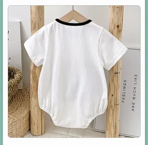 Detail of baby cotton romper with black neck trim hanging on a wooden stand