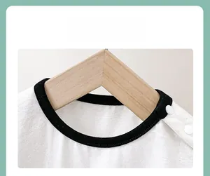 Detail view of baby bodysuit with shoulder snaps and black contrast neckline on wooden hanger