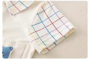 Detail of white cotton baby romper with rainbow plaid trim and cartoon animal embroidery