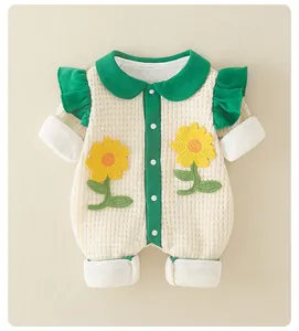 Detail of cream waffle knit baby romper featuring green ruffles and sunflower crochet patches
