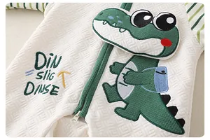 Close-up of quilted baby romper fabric with green crocodile embroidery and zipper detail