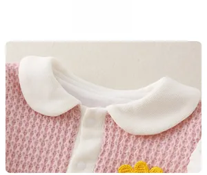 Close-up of pink waffle knit baby bodysuit with white collar and yellow crochet flower