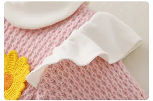 Detail of pink knitted infant romper with white ruffle trim and yellow sunflower patch