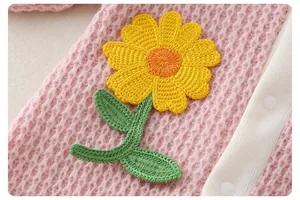 Close-up of pink knit baby romper with yellow sunflower embroidery and white snap buttons