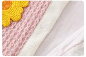 Detail of pink waffle knit baby romper with yellow sunflower crochet and white snap buttons