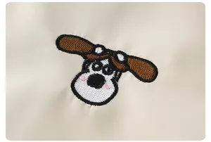 Detailed close-up of cute cartoon dog embroidery on the cream white kids' jacket