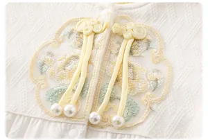 Macro detail of baby romper showing Ruyi button, floral embroidery, and waffle fabric