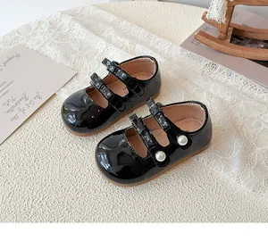 Détail de babies en cuir verni noir avec doubles brides et accents de perles
