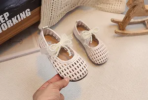Dettaglio della trama intrecciata su scarpe crema da bambina con fiocco di pizzo e perle
