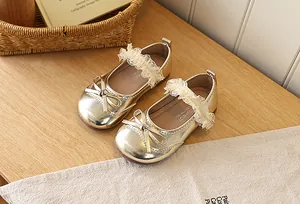 Detail of golden Mary Jane girl shoes with bow, lace strap and shiny metallic finish