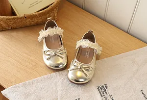 Top view of gold Mary Jane girls shoes with bow and cream lace strap on rustic background