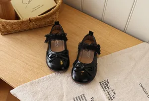 Close-up of black patent leather girls Mary Janes with bow and lace trim on wood