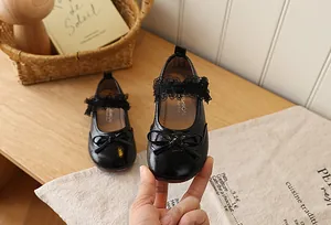 Detail of glossy black girls leather shoes with bow decoration and lace strap
