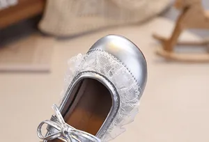 Nahaufnahme silberner Baby-Mary-Janes mit feiner Spitze und eleganter Schleife