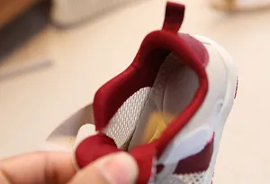 Detailed close-up of breathable mesh fabric and red padded heel lining of kids sneakers