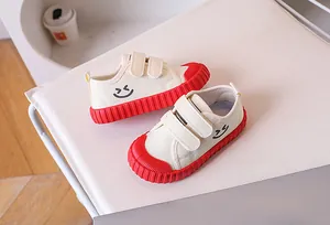 Detail view of cream canvas kids shoes with red rubber sole and smiley face print