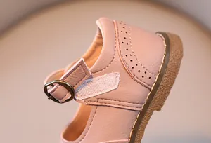 Detail of pink girls' leather shoes with brogue patterns and adjustable velcro buckle