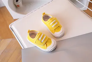 Close-up of yellow canvas kids shoes with white elastic straps and reinforced rubber toes