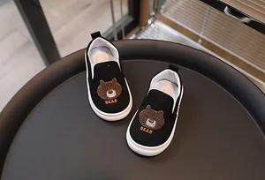 Gros plan sur chaussures en toile noires enfant avec broderie ours et semelle blanche antidérapante