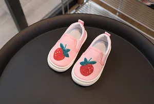 Détail de chaussures en toile rose pour enfants avec broderie fraise rouge sur plateau noir