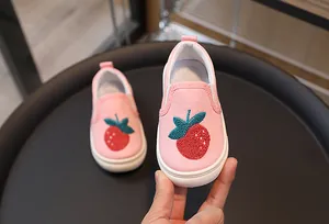 Gros plan d'une broderie fraise sur chaussures en toile rose avec semelle blanche