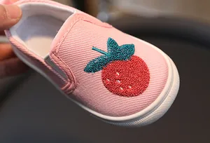 Détail de la chaussure en toile rose pour bébé avec broderie fraise et semelle gomme
