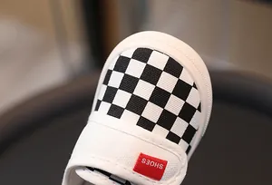 Detail of checkered canvas kids' shoe with a red 'SHOES' tag and anti-collision toe