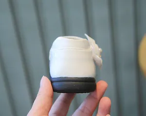 Détail de chaussures blanches pour filles en cuir verni avec fleur 3D et perle élégante